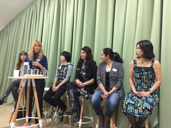 Panel of women presenters sitting on high stools in front of a green curtain