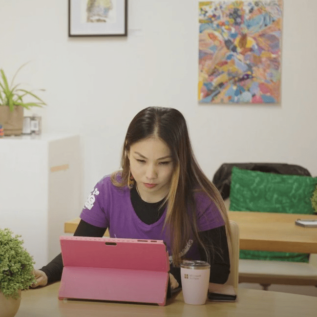me, sitting at table typing on a pink laptop