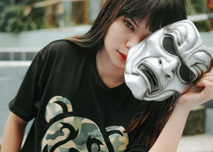 woman holding a silver mask slightly in front of her face