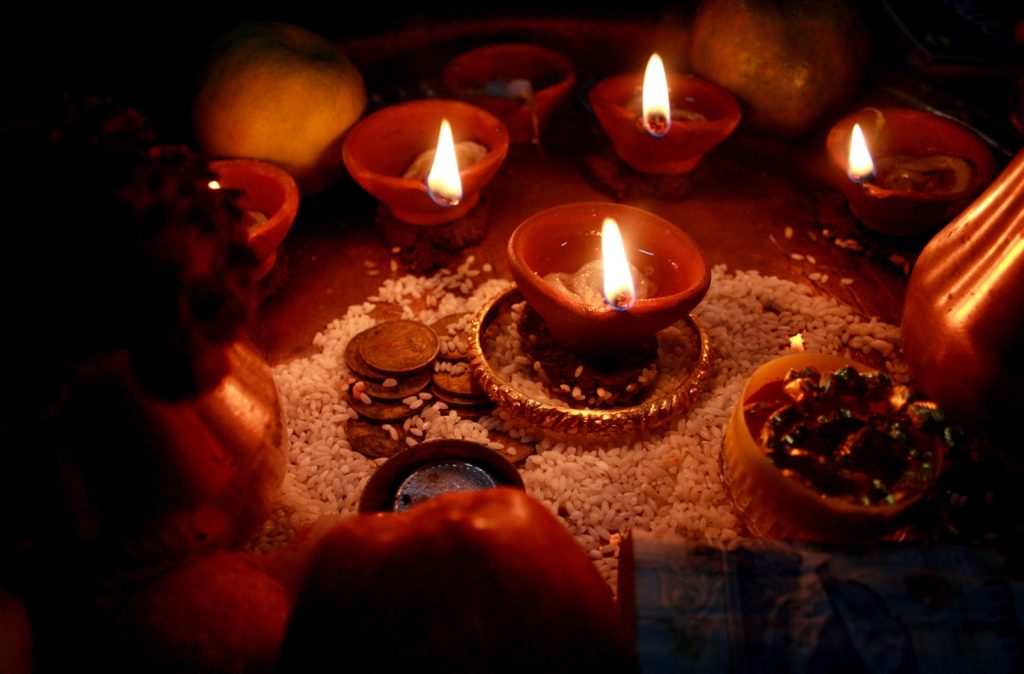 A largely decorative photo showing several clay lamps, usually used during traditional Indian pooja (prayers). The clay lamps have an oil wick and are sitting on rice and coins.