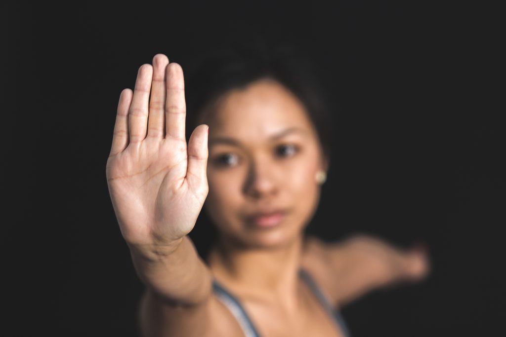 Largely decorative image. Black background with an woman holding her hand up to the camera. The hand is in focus, and the woman is slightly blurred
