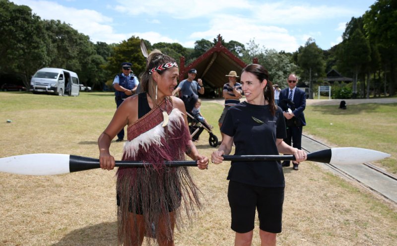 Photograph of then Prime Minister Jacinda Ardern standing next to a Māori woman in traditional dress holding a large paddle.