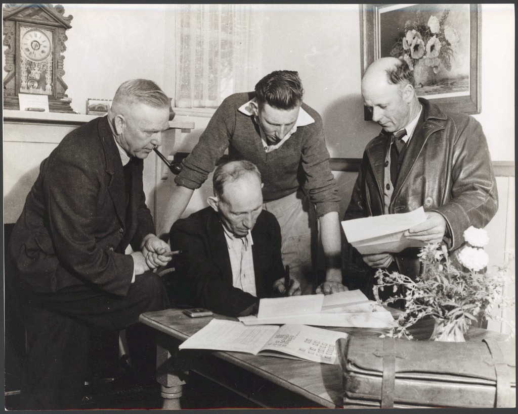 Old sepia photograph of four white men signing something on a table
