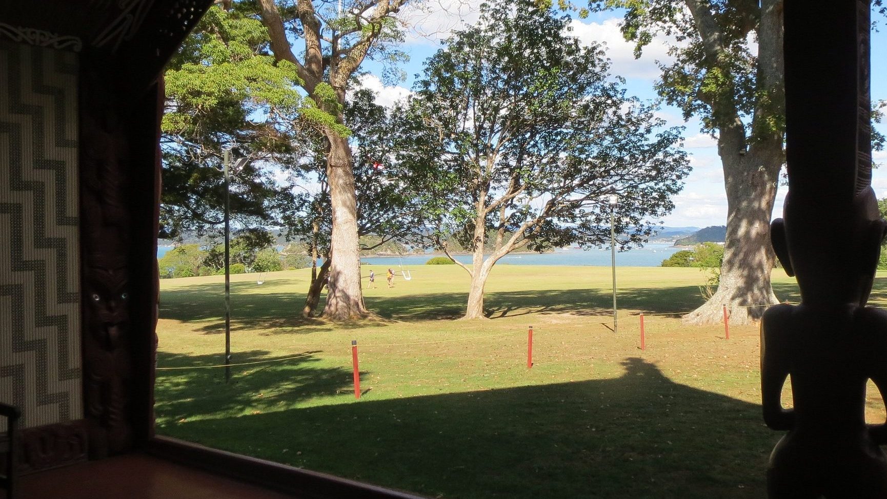 A largely decorative image looking out from a wharenui (traditional Māori meeting house) onto the lawn at Waitangi Te Tiriti grounds