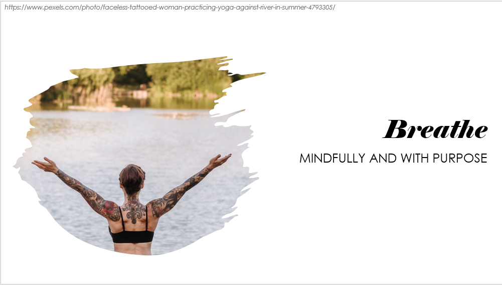 Largely decorative image of the back of a tattooed person with their arms outstretched. You can see a lake vista, blurrily, in front of them. The words say "Breathe, mindfully and with purpose"