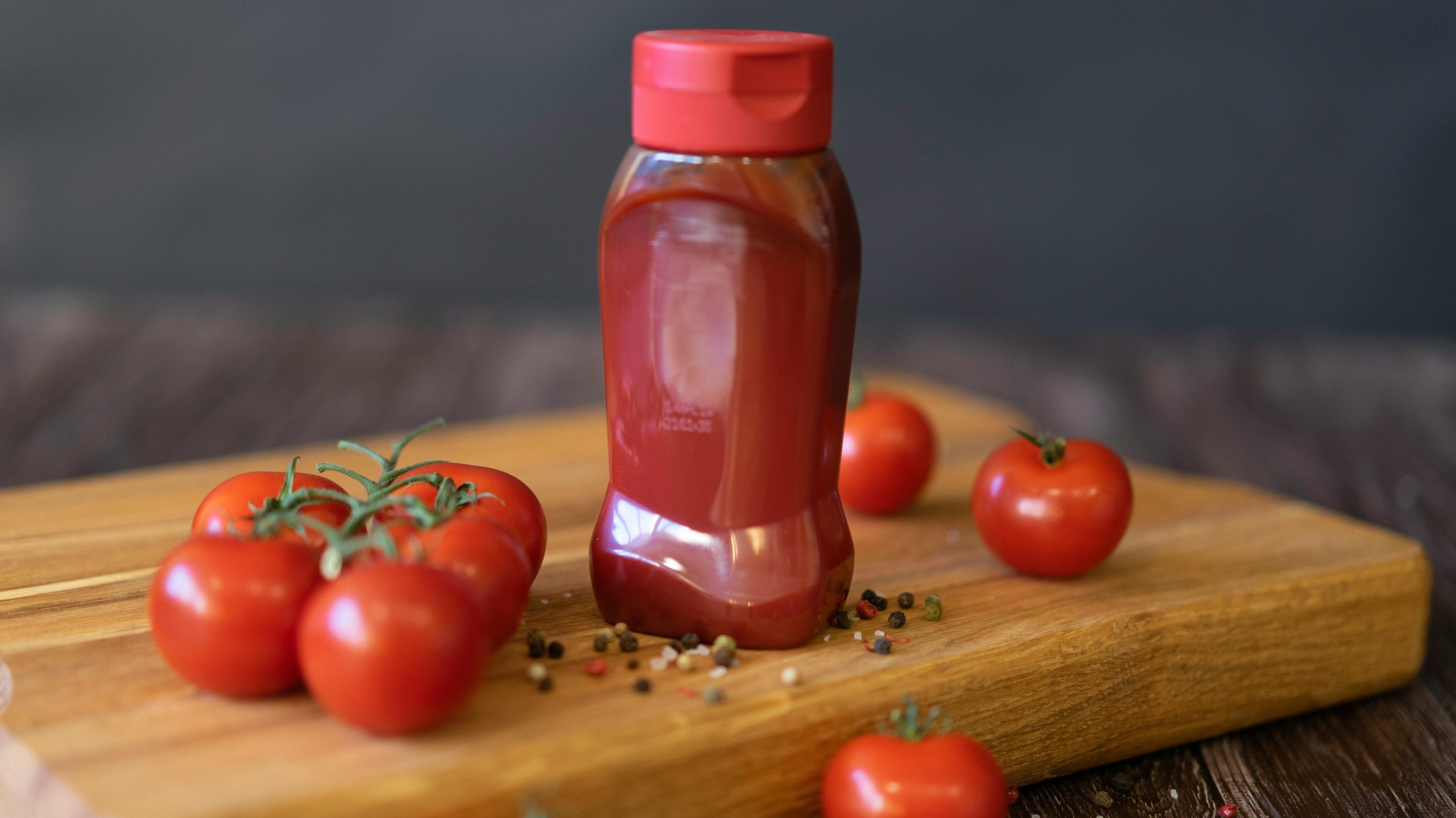 Largely decorative image of a sauce bottle sitting on a wooden board with fresh tomatoes scattered around the bottle.