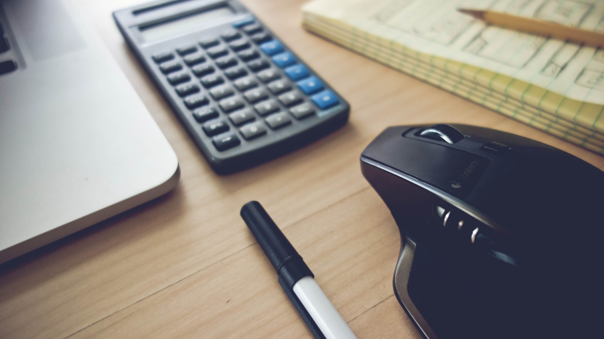 A largely decorative photo of a desk with a calculator, a notepad, a pencil, a pen and a mouse