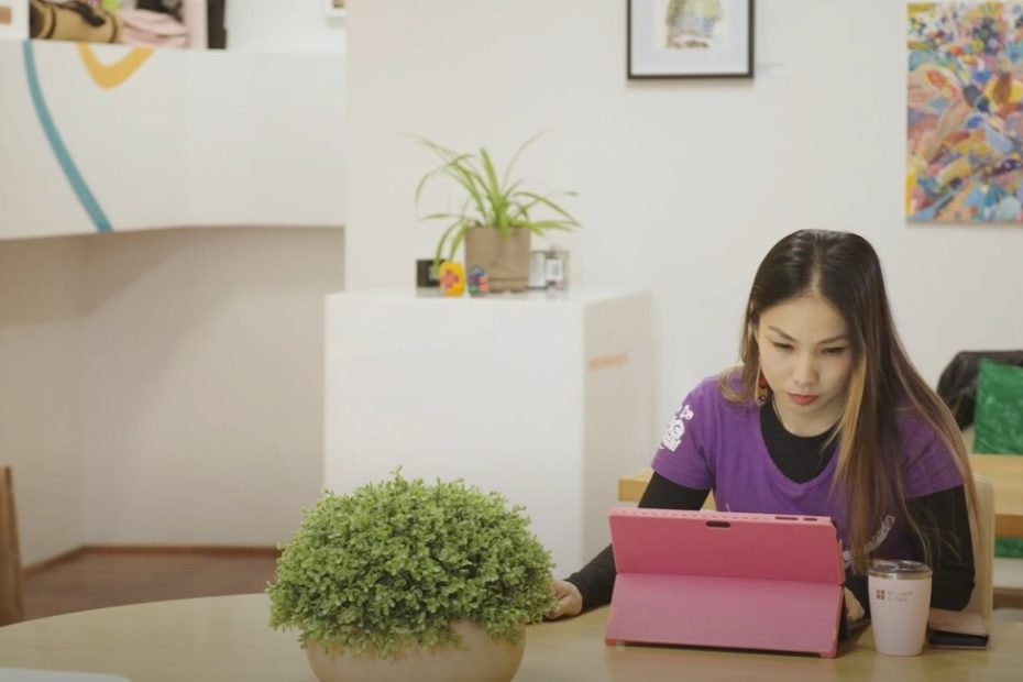 Largely decorative still from the video. It is me sitting at a table surrounded by plants with a pink laptop in front of me