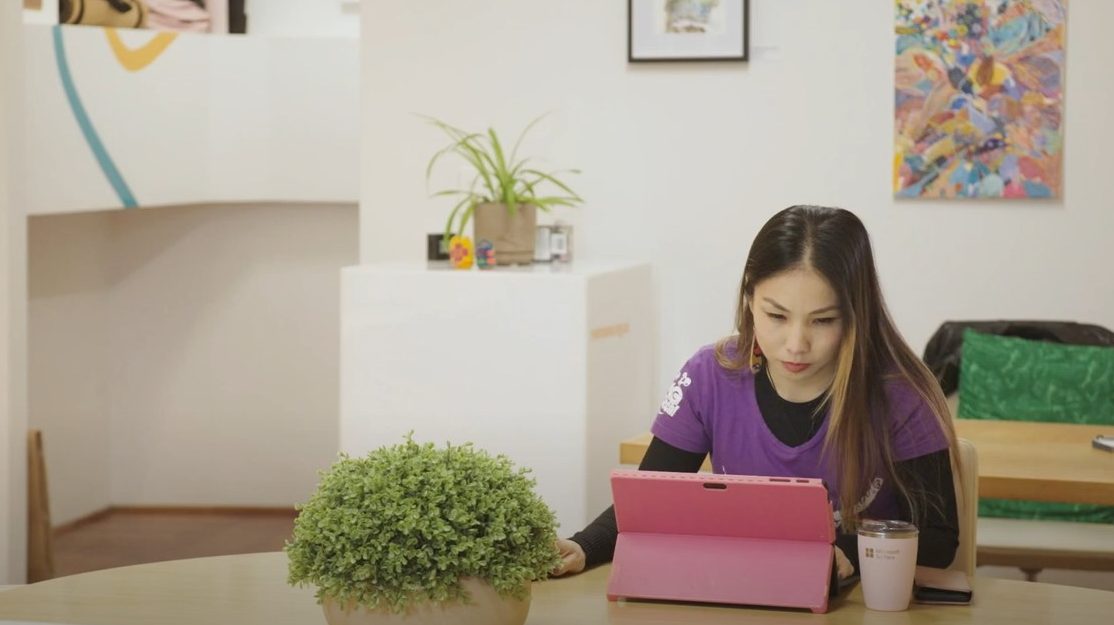 Largely decorative still from the video. It is me sitting at a table surrounded by plants with a pink laptop in front of me