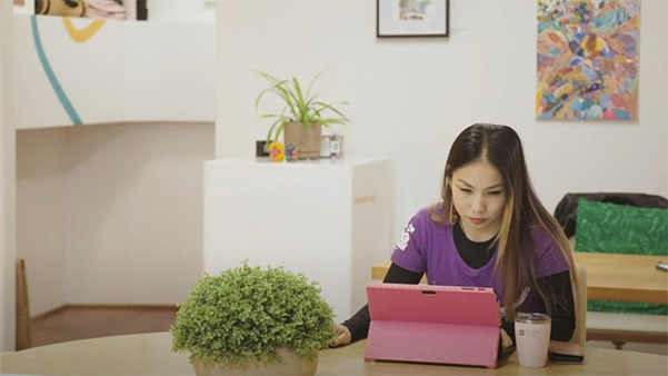 Largely decorative image of me sitting at a desk with a pink laptop. I am surrounded by art and plants